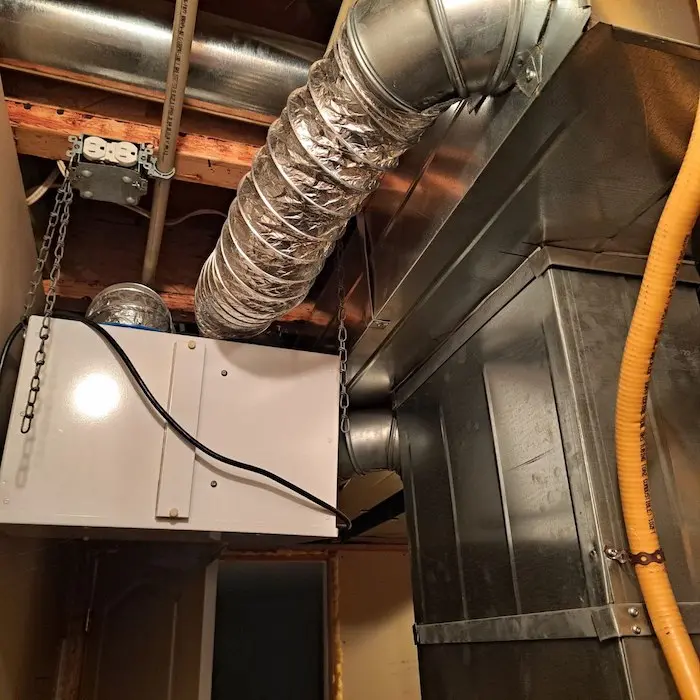 A modern Energy Recovery Ventilator (ERV) unit installed in a home mechanical room with duct connections