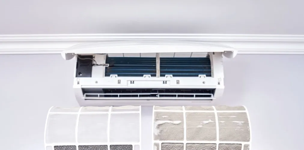 A wide shot of the indoor AC unit with its cover lifted and filters removed. Below it, the two detached filters are visible, showing a significant accumulation of dirt and debris.