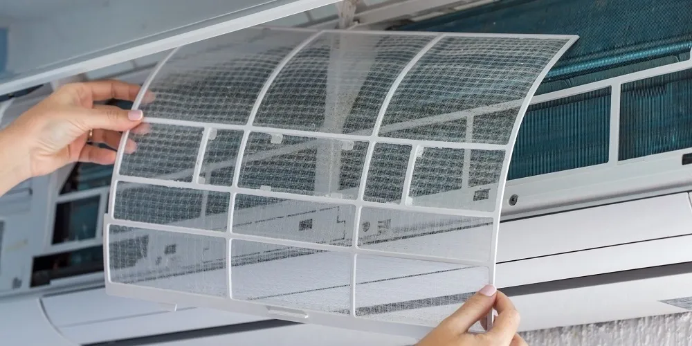 A person is shown reinserting a clean, translucent mesh filter back into the air conditioning unit after it has been washed and dried.